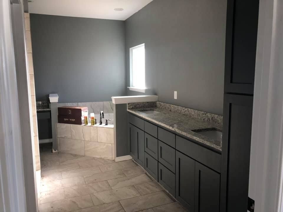 Bathroom with gray walls, cabinets, and stone countertops; a tub and window are also visible.