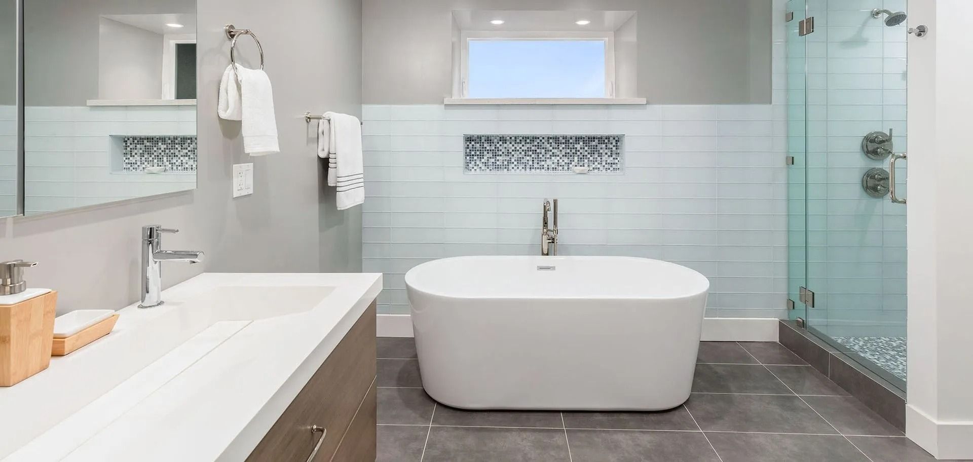 Modern bathroom with white tub, glass shower, and gray tile flooring.