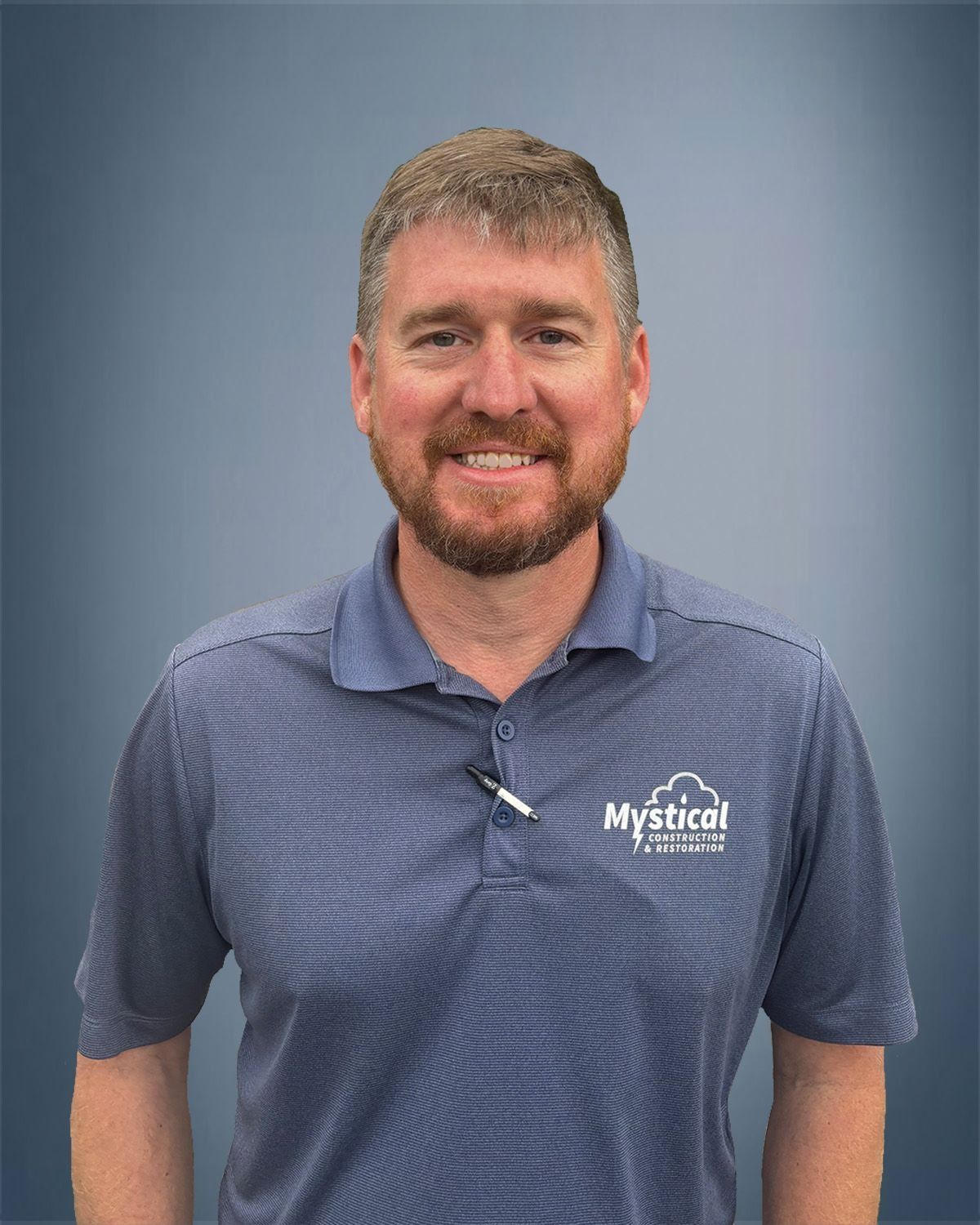 Man with short brown hair and beard, wearing a blue polo shirt, smiling, with a gray background.