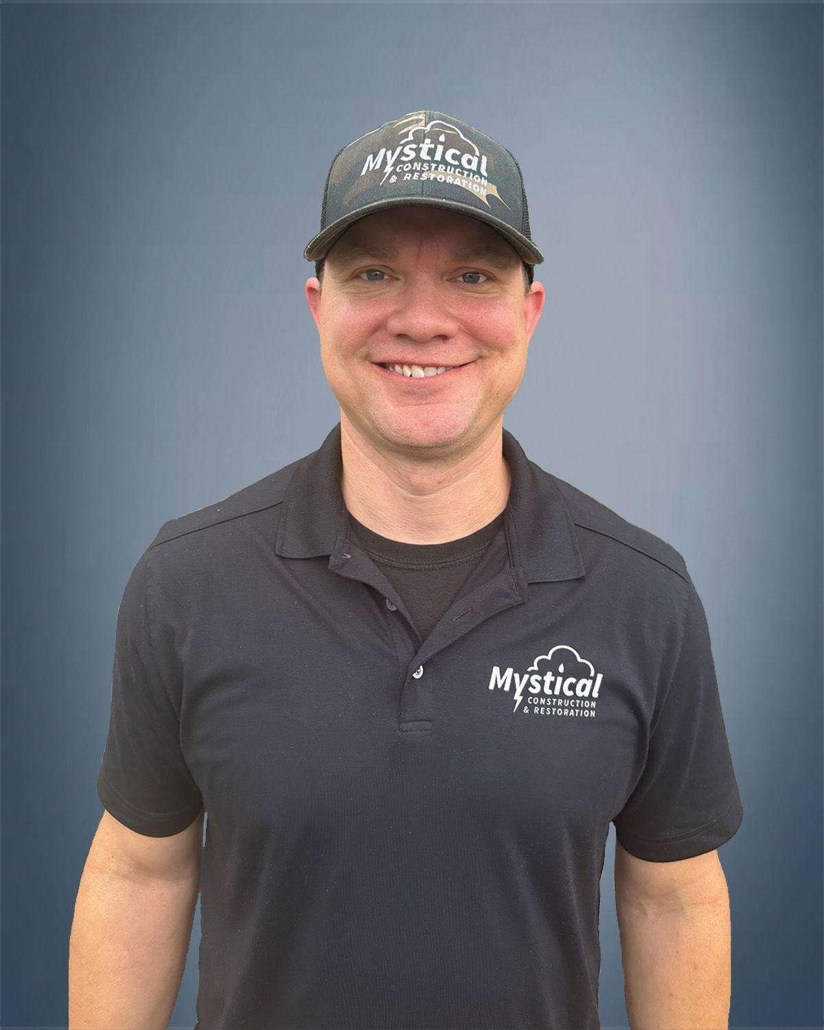 Man wearing a black hat and shirt with a company logo, smiling. Blue background.