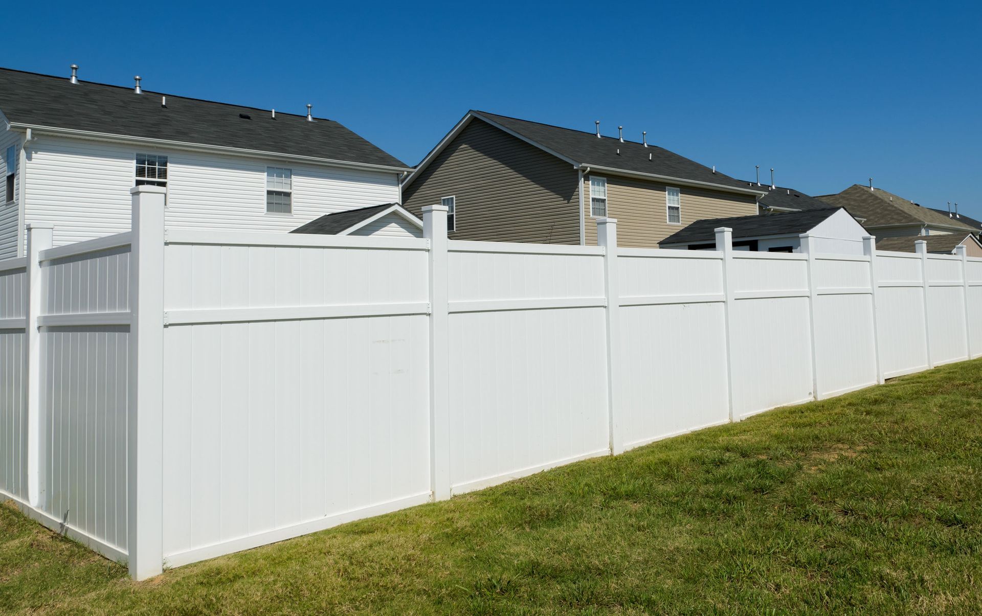White vinyl privacy fence along a grassy yard beside suburban houses.