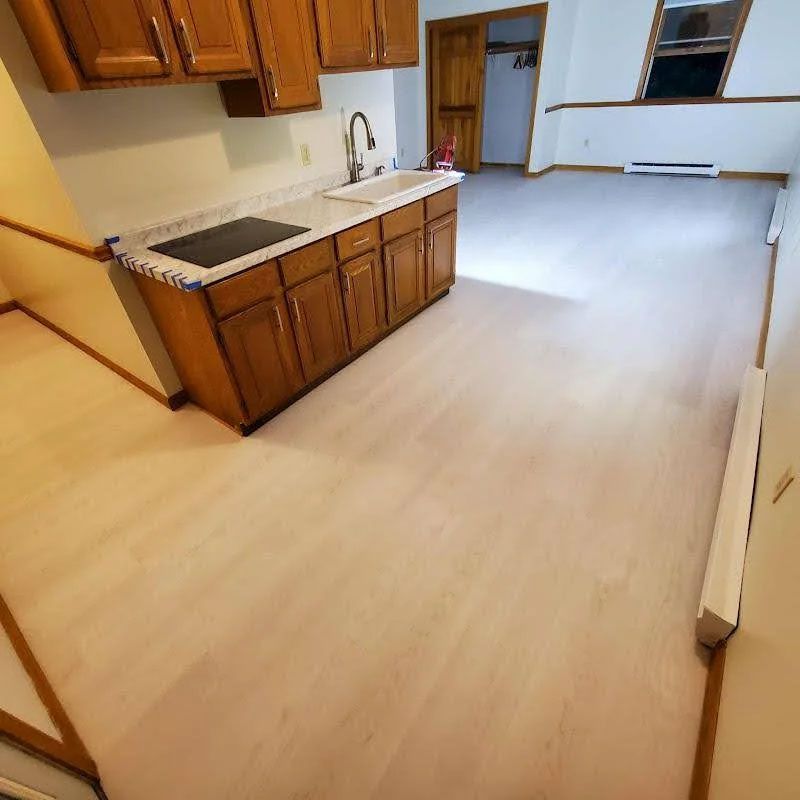 Empty kitchen with wood cabinets, white counters, and light-colored flooring in a spacious room