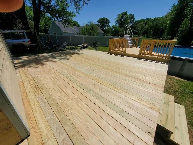 Wooden backyard deck under construction beside a fenced yard on a sunny day