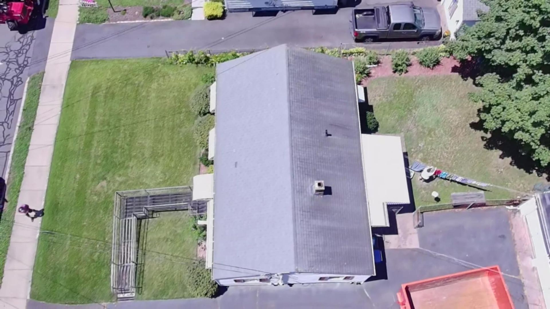 Aerial view of a gray-roofed house with a lawn, driveway, and neighboring street