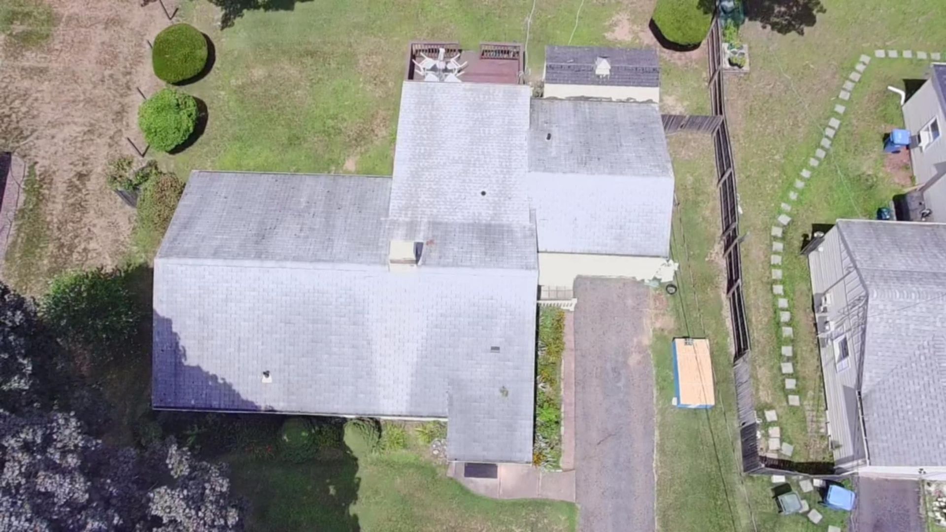 Aerial view of a house with gray roofs, backyard lawn, and a small shed beside a neighboring home.