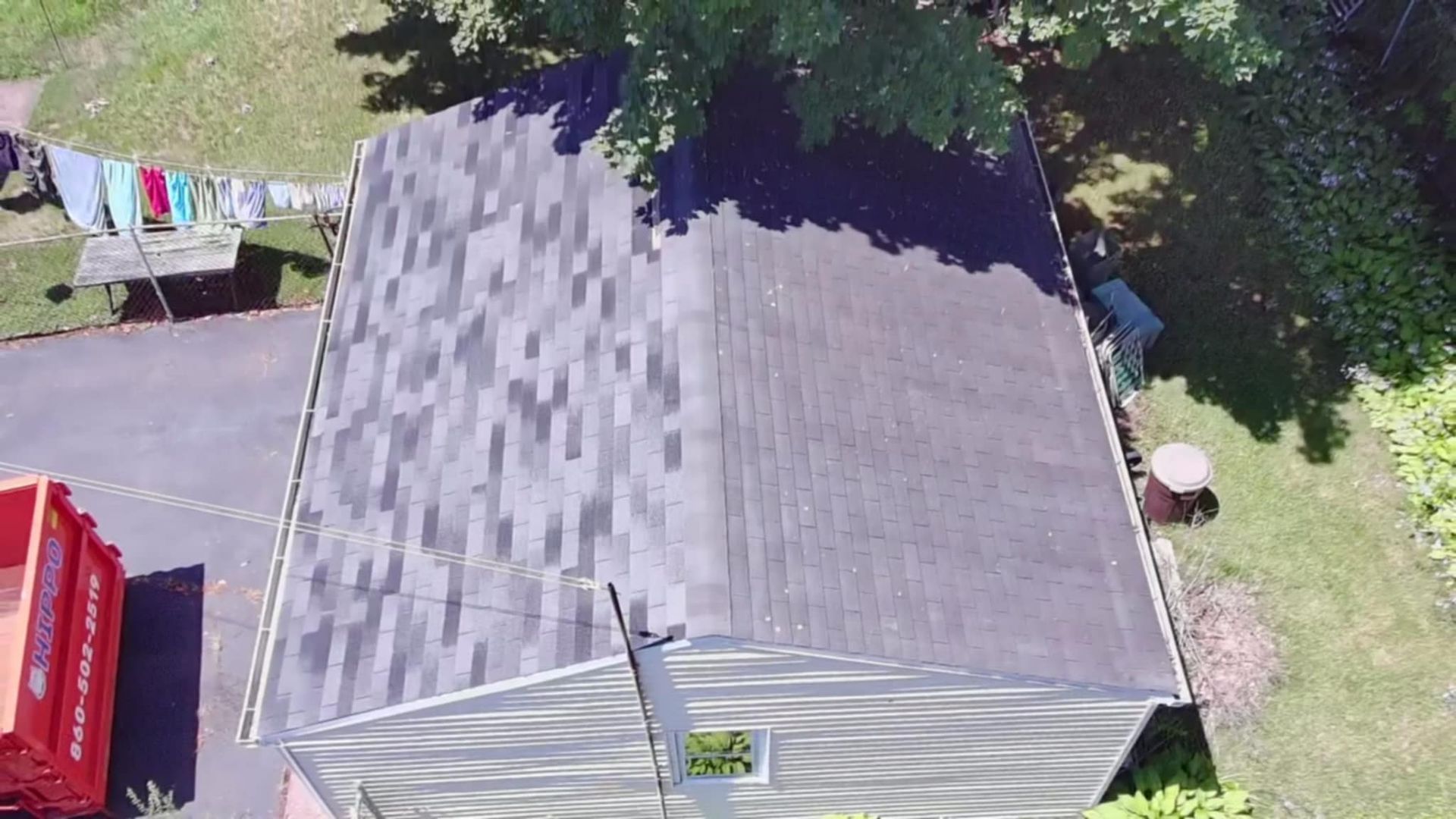 Aerial view of a gray-roofed shed beside a red vehicle, with trees and a clothesline nearby.