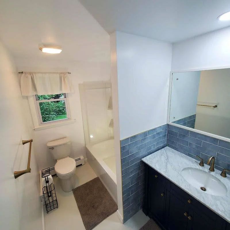 Bright bathroom with toilet, shower, and dark vanity with blue tile backsplash and mirror