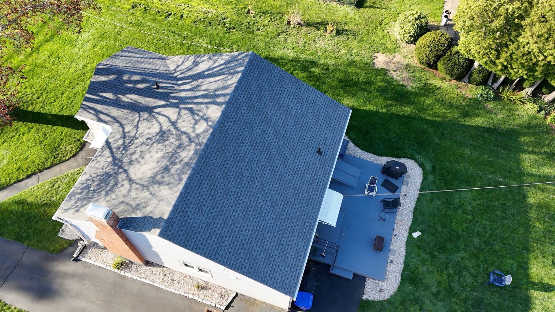 Aerial view of a gray-roofed house with a driveway, patio furniture, and green lawn.