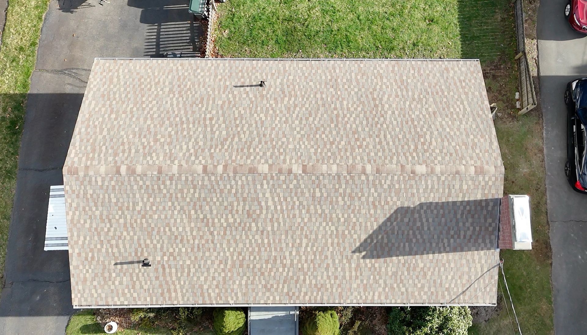 Aerial view of a beige shingled house roof with shadows and grass around it