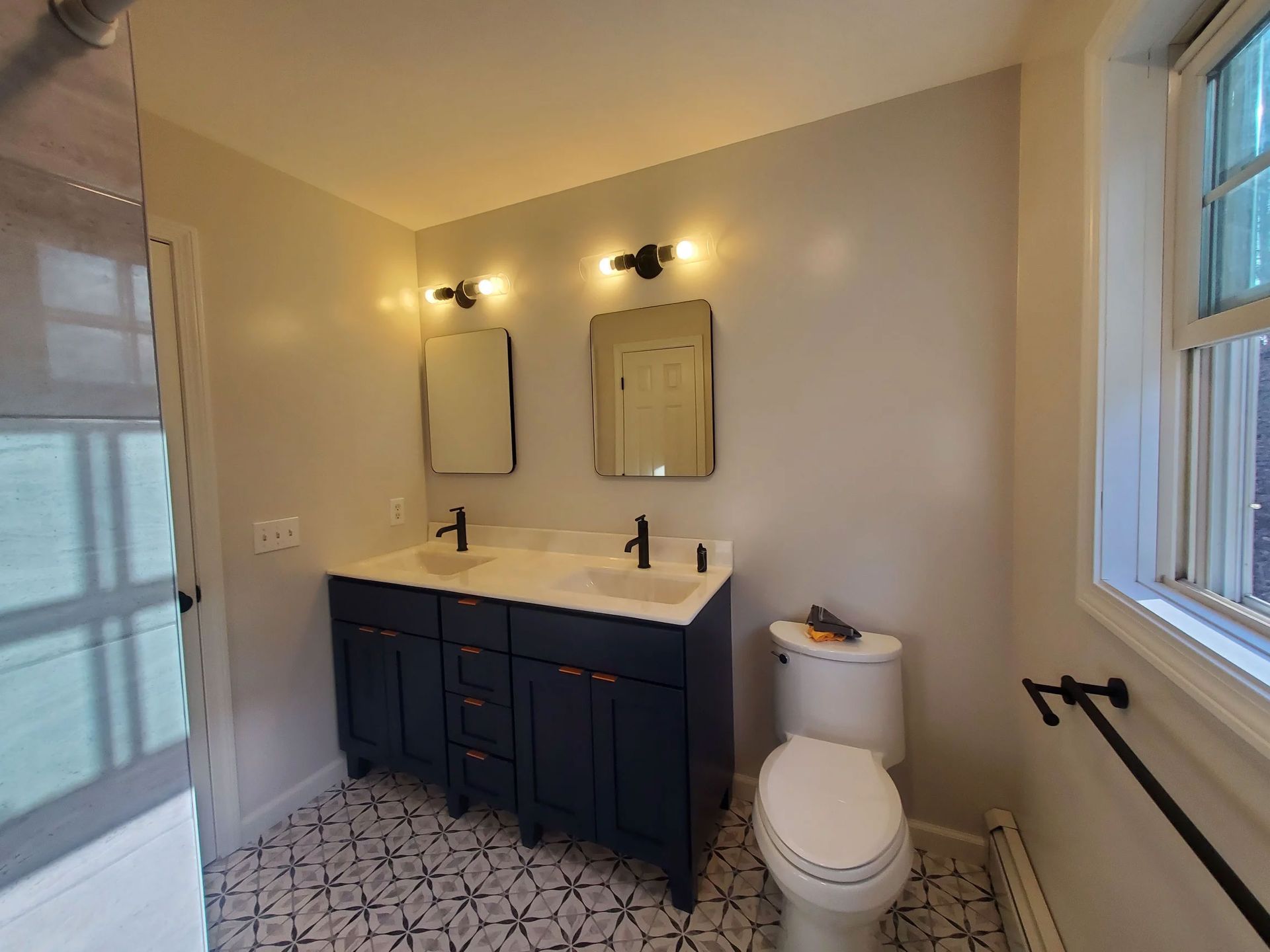 Small bathroom with navy vanity, white sink, mirror, toilet, and shower with glass door
