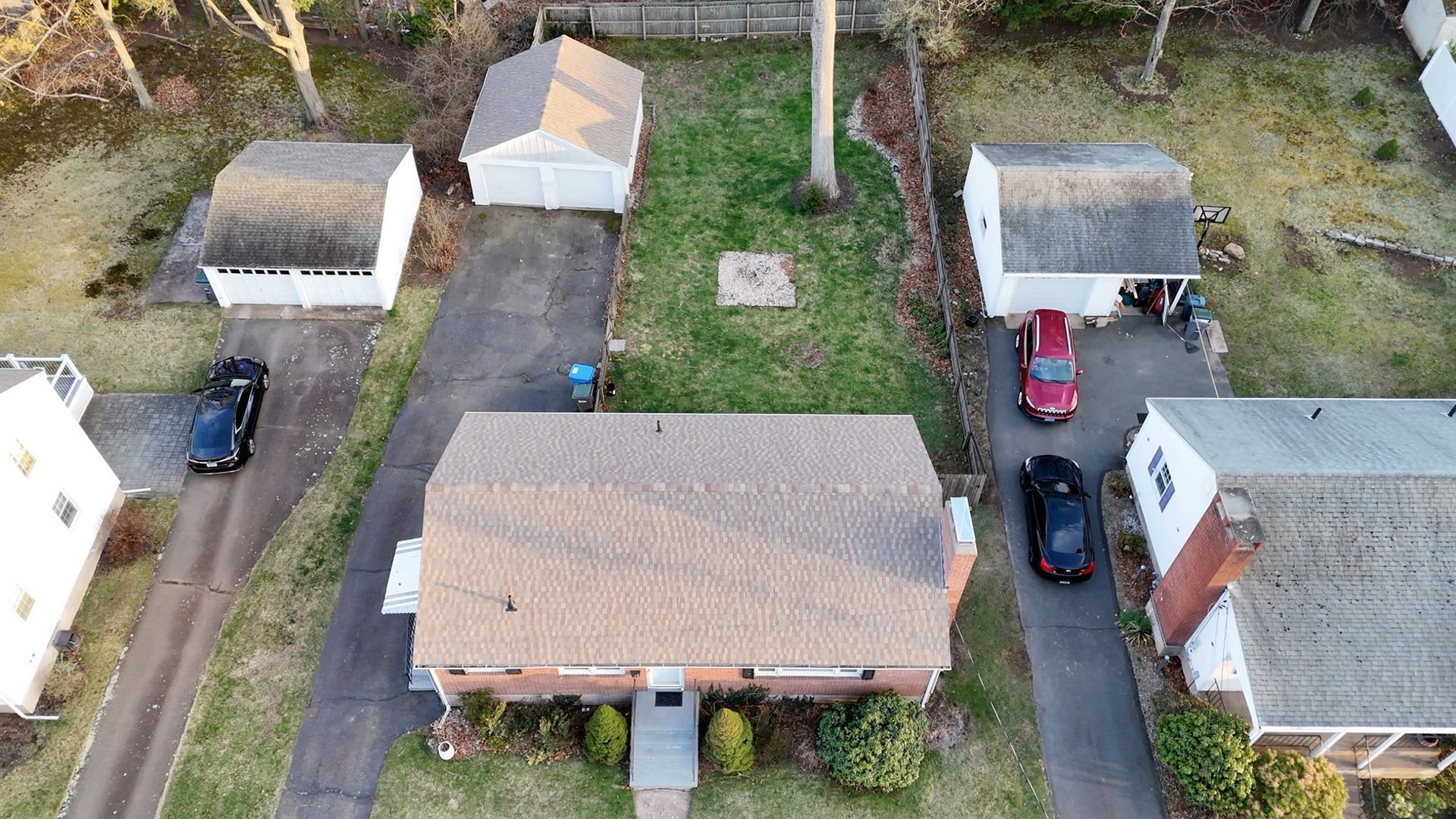 Aerial view of suburban homes with driveways, parked cars, and a grassy neighborhood yard.
