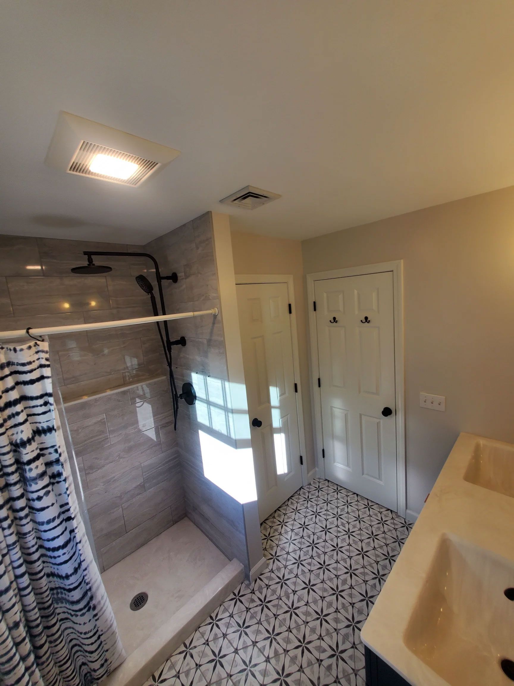 Bathroom with tiled shower, patterned floor, white cabinet doors, and a beige vanity under bright ceiling light