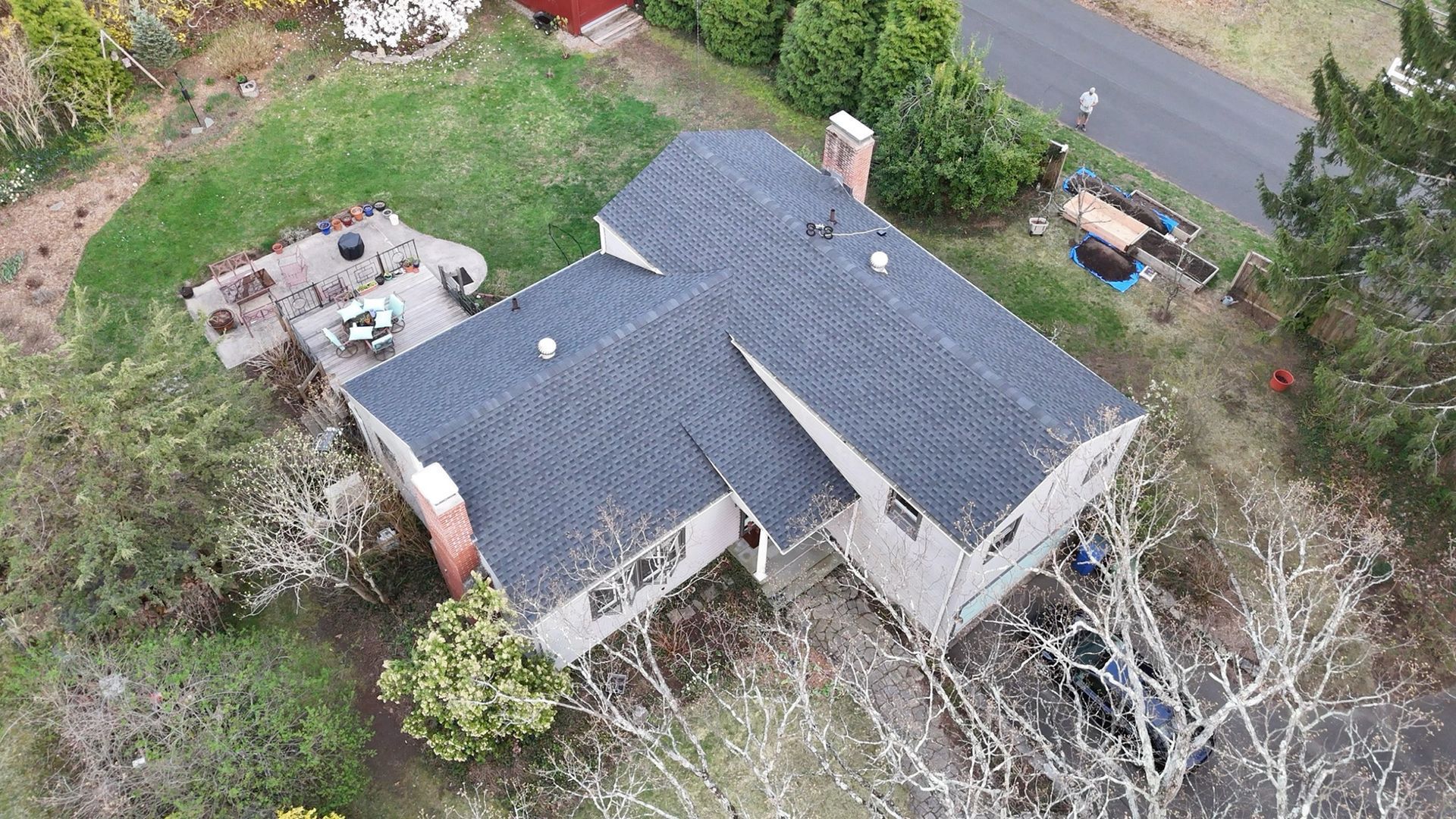 Aerial view of a house with a dark roof, driveway, and trees surrounding the property.