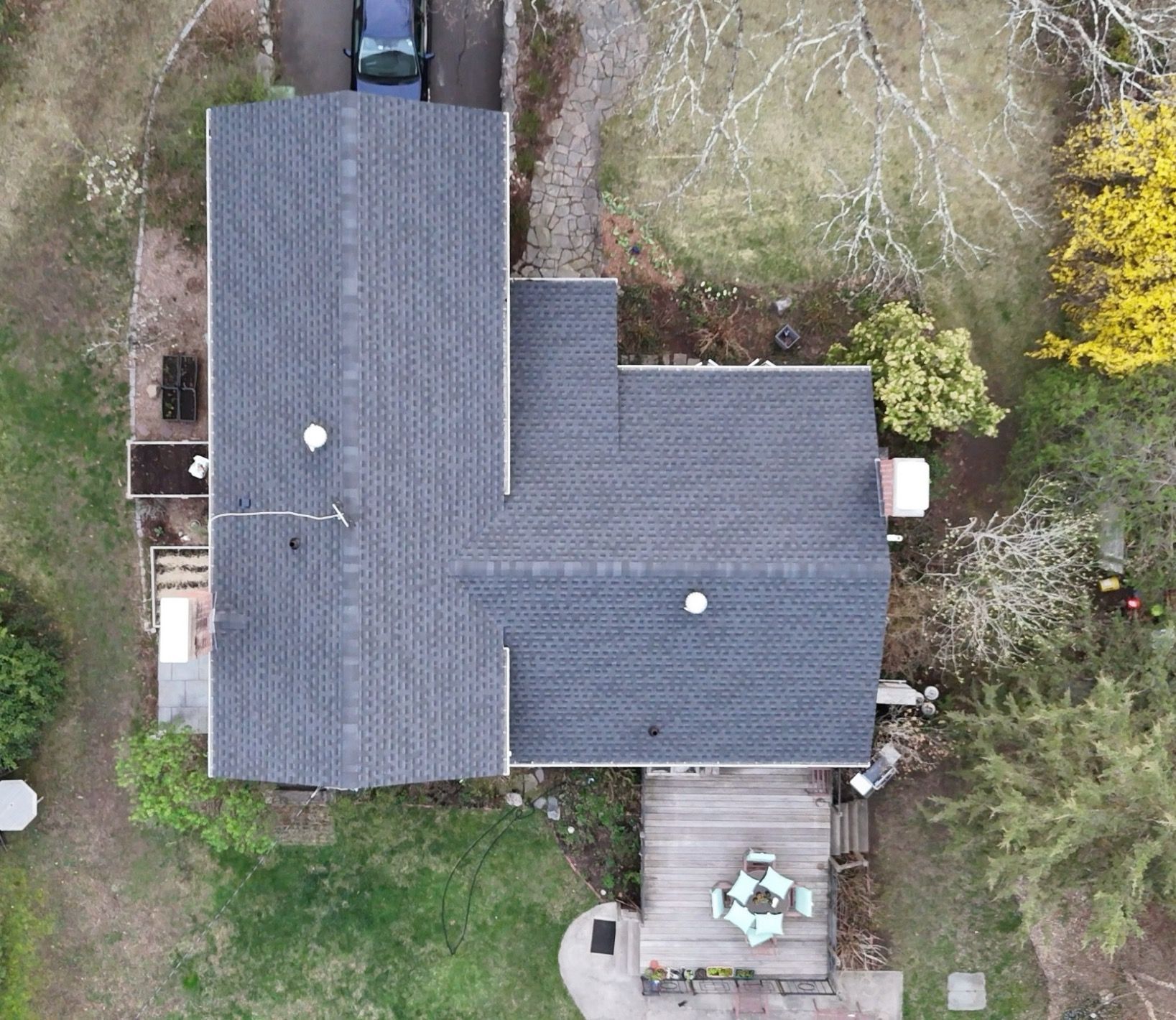 Aerial view of a house with a dark gray roof, surrounding trees, and a small patio area