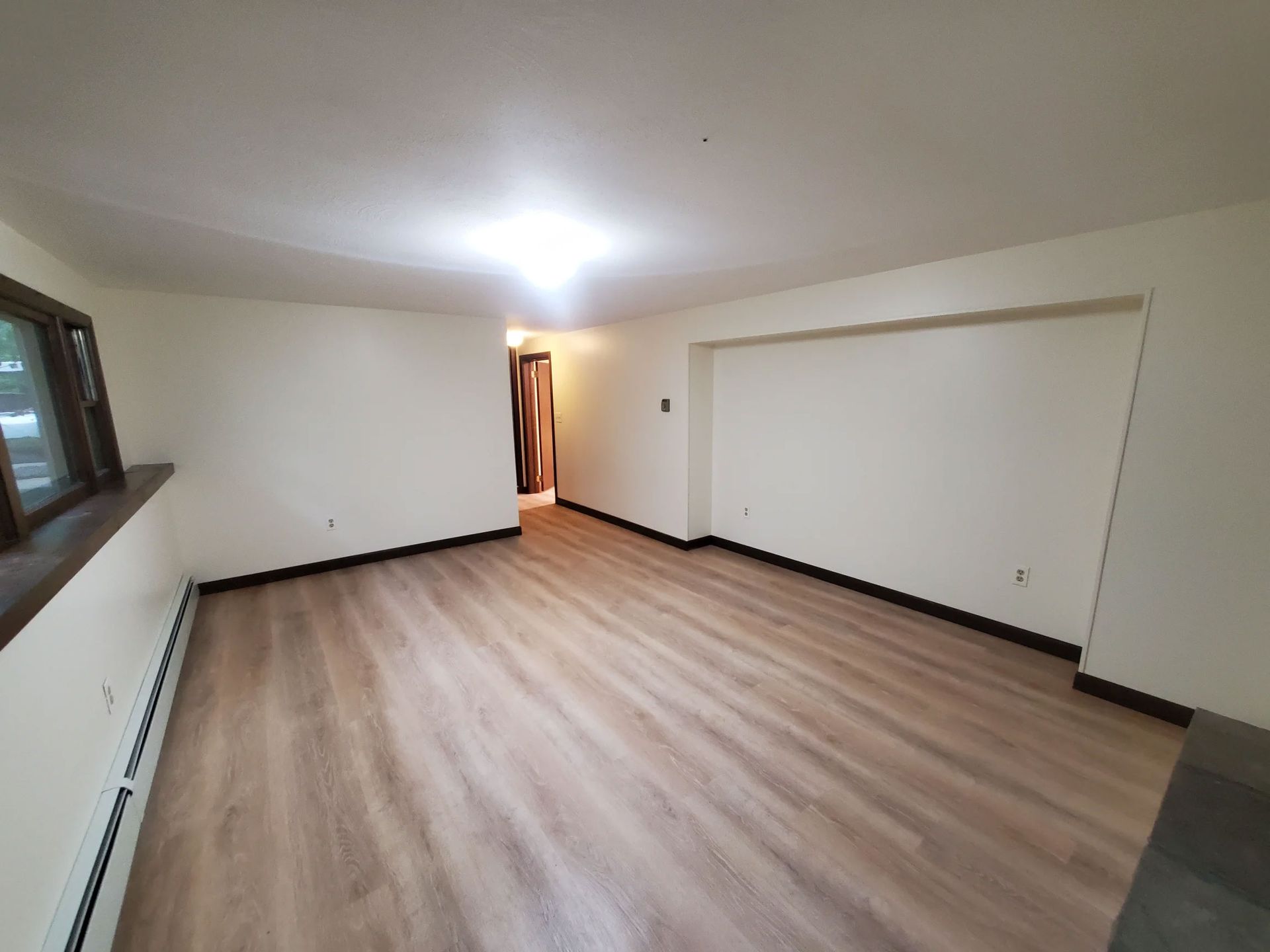 Empty unfurnished room with light wood flooring, white walls, and a bright ceiling light.
