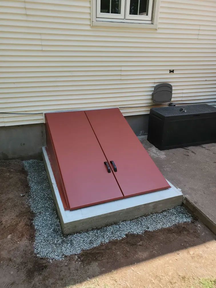 Red double-access hatch beside a house wall, framed by gravel and concrete.