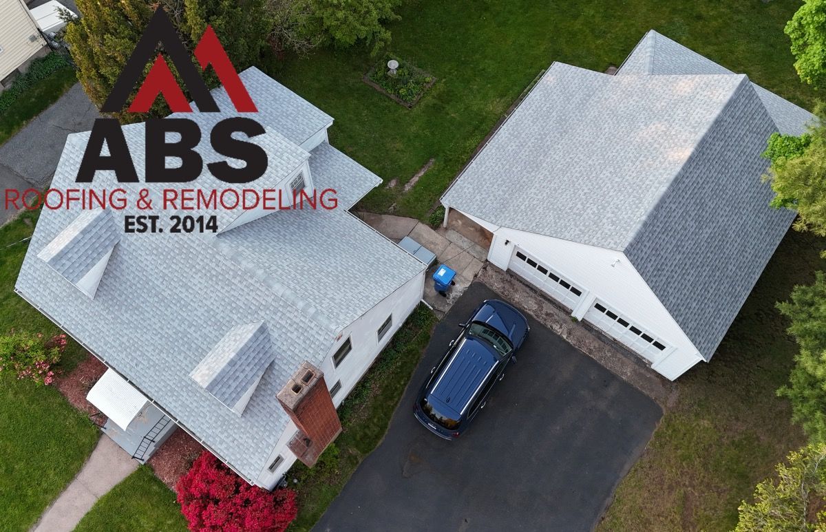 Aerial view of two gray-roofed houses and a blue car with ABS Roofing & Remodeling logo overlay.