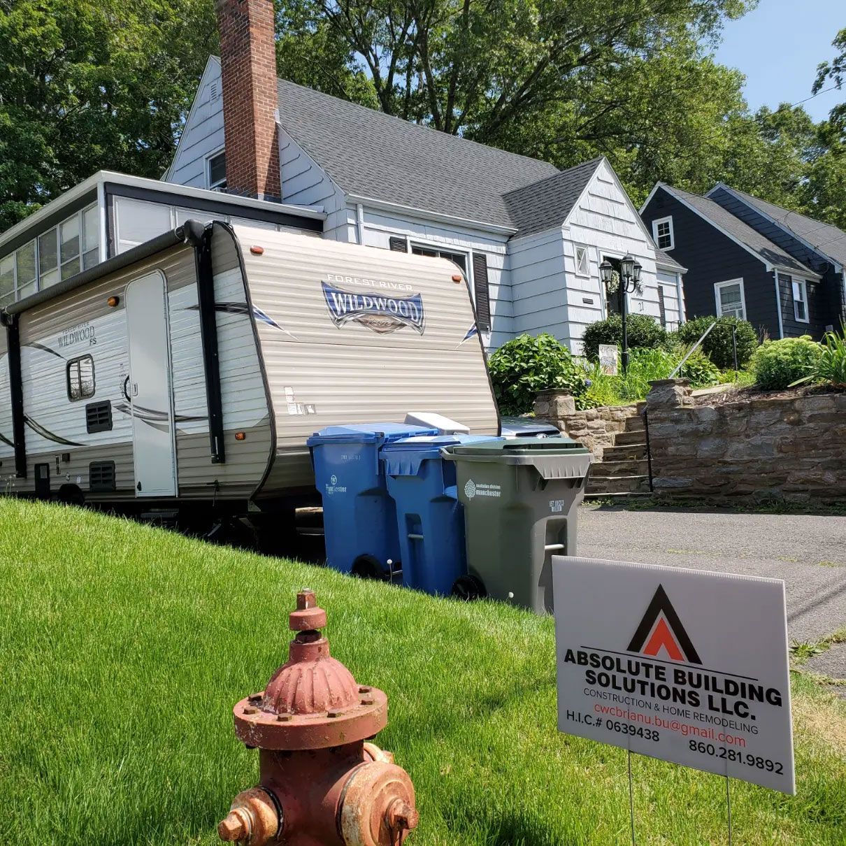 RV parked beside a house with trash bins, a fire hydrant, and a construction sign in the foreground