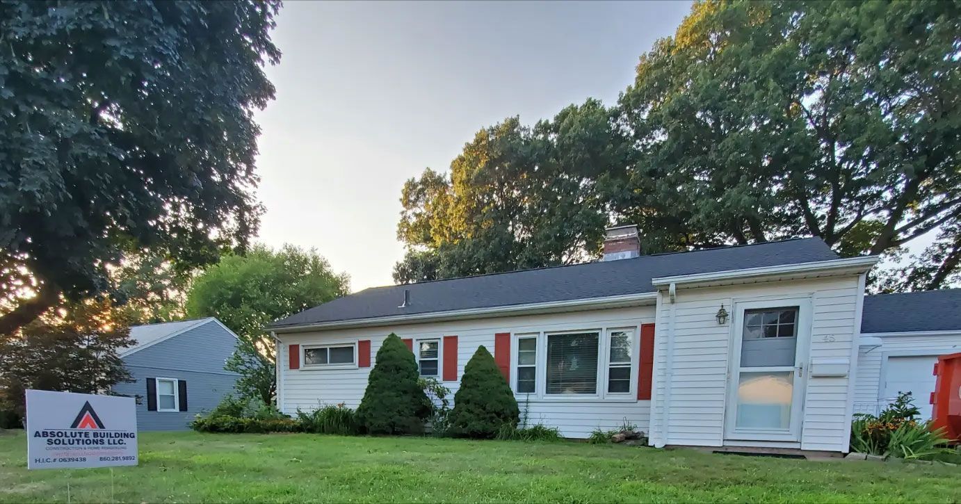 Single-story white house with red shutters and a front lawn, with a yard sign in the foreground.