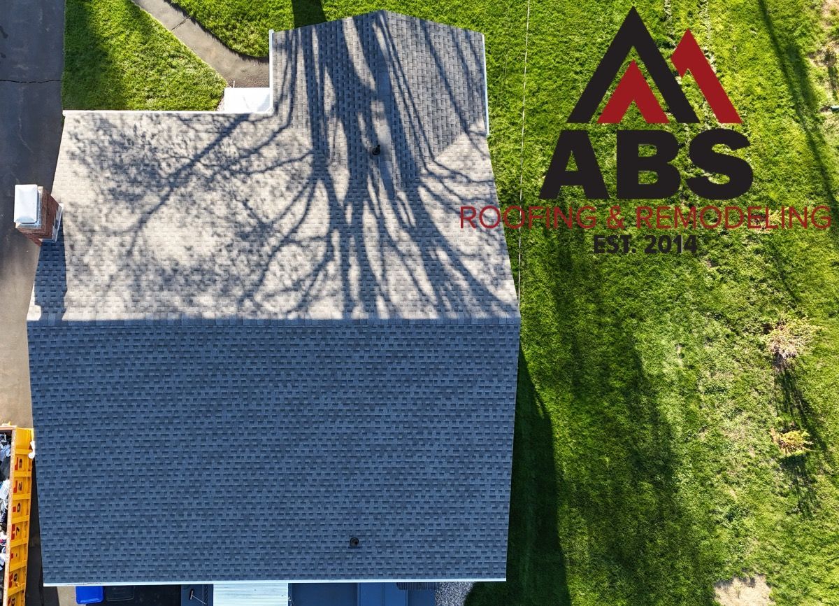 Aerial view of a house with a dark blue roof, surrounded by grass and a driveway, with an ABS logo nearby