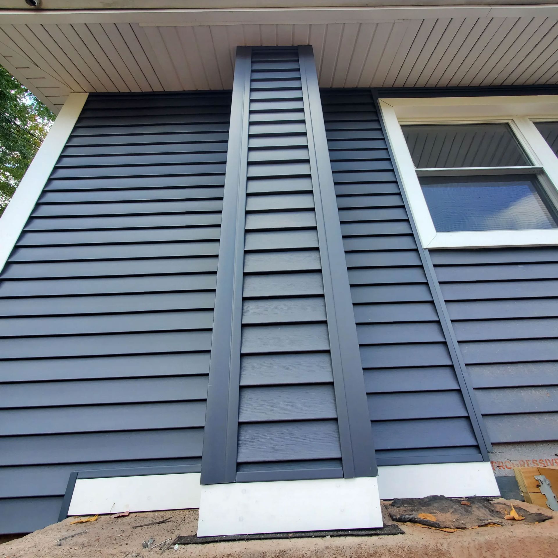 Vertical black siding trim on a house exterior beneath the eaves, with a window on the right