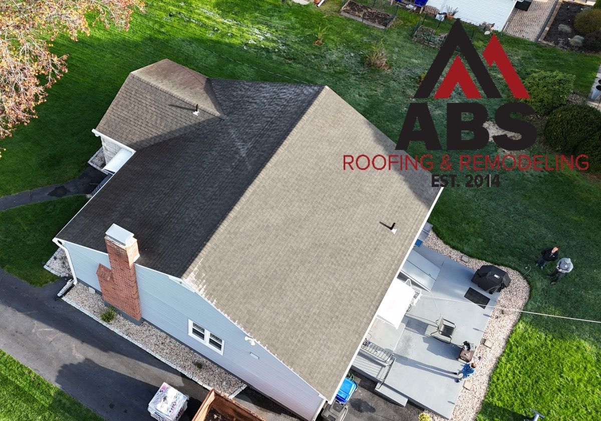 Aerial view of a gray-roofed house with a small deck and driveway, beside a lawn and trees.