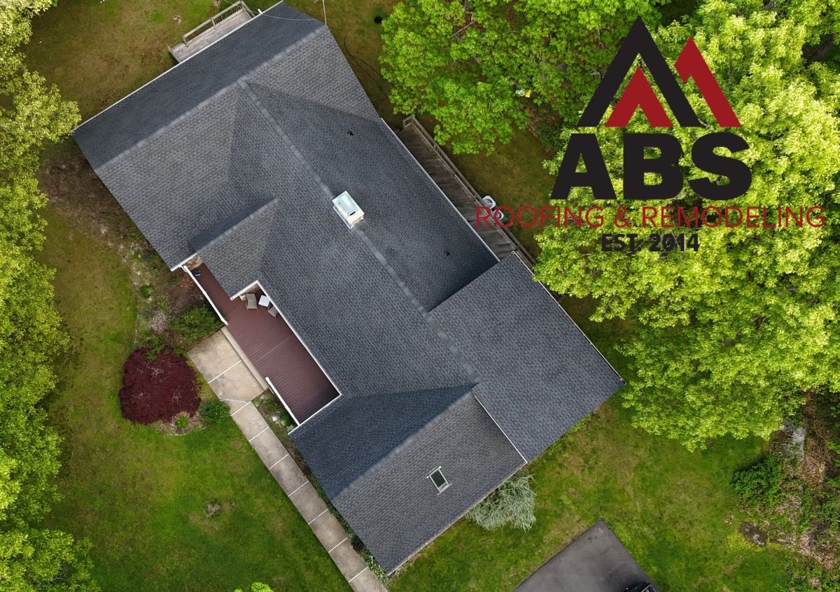 Aerial view of a house with gray roof beside green trees and an ABS logo watermark