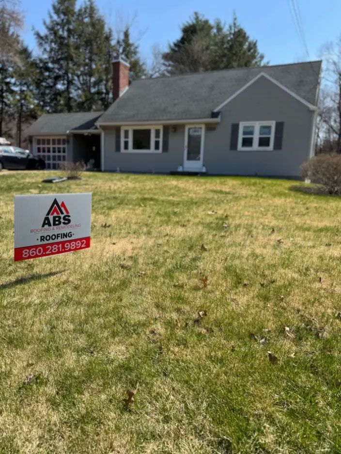 Gray house with white trim and an ABS roofing sign in the front yard