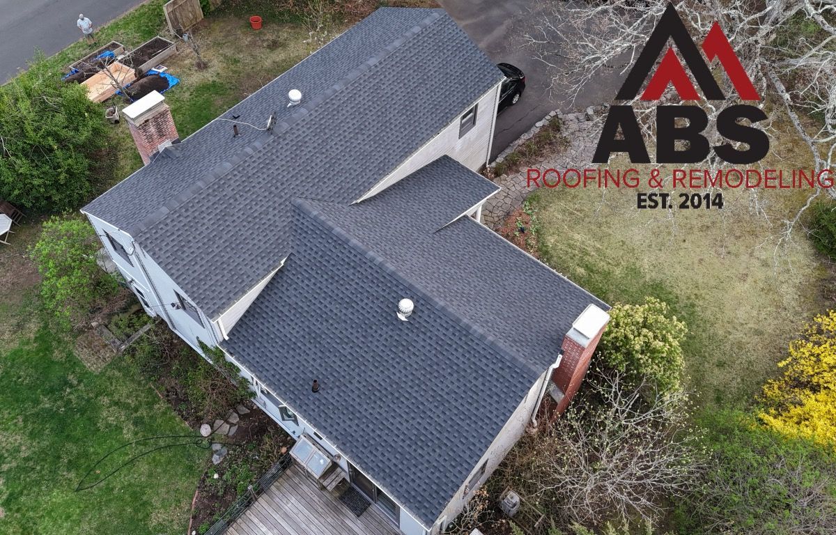 Aerial view of a house with a dark gray roof and surrounding trees, with ABS Roofing logo watermark.