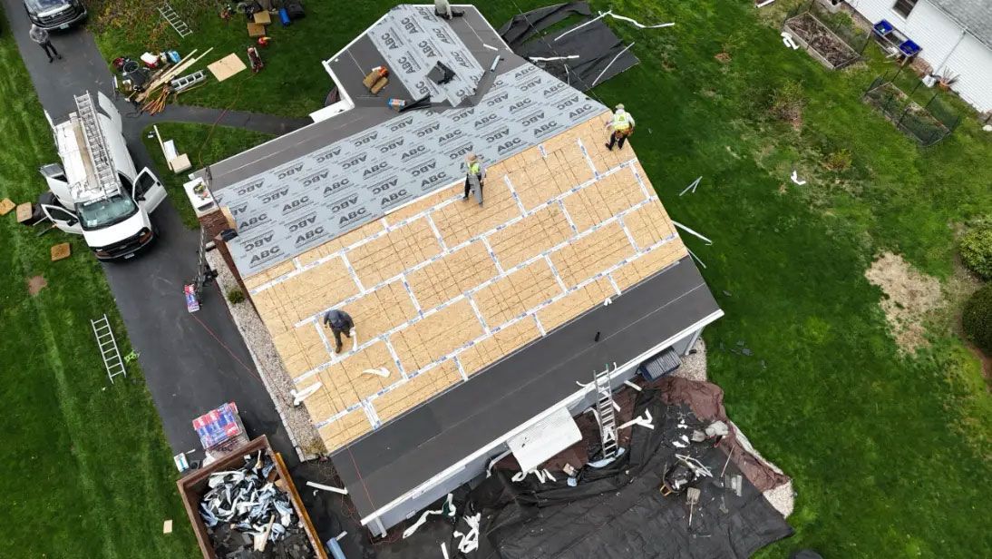 Aerial view of a roof under construction with gray and tan roofing materials and a crane nearby.