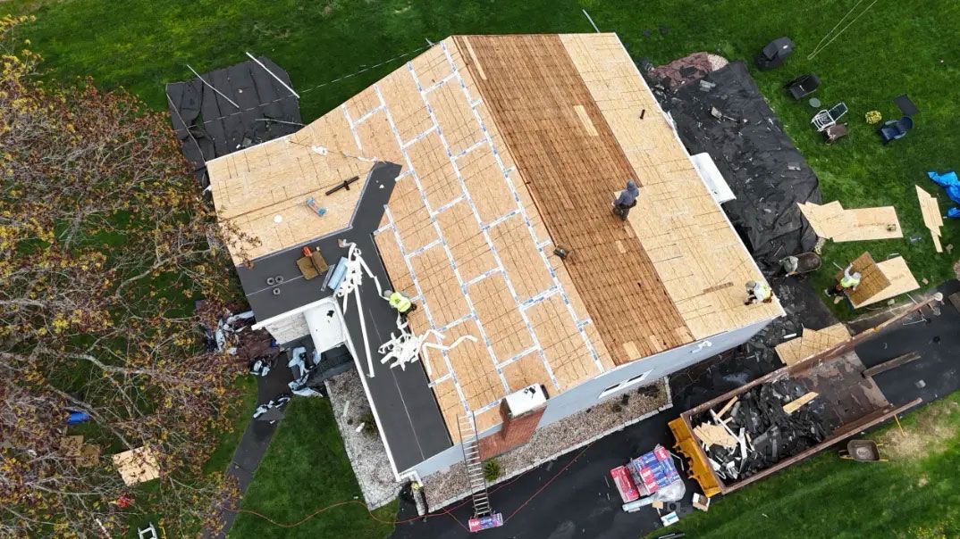 Aerial view of a house with a partially replaced roof and surrounding yard area