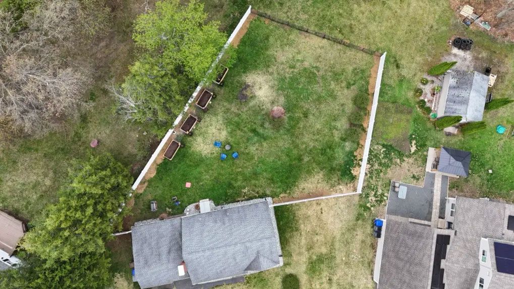 Aerial view of a fenced backyard with grass, a house roof, and a small shed or outbuilding
