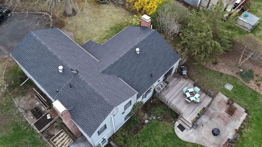 Aerial view of a house with a dark roof and a patio with outdoor furniture beside it.