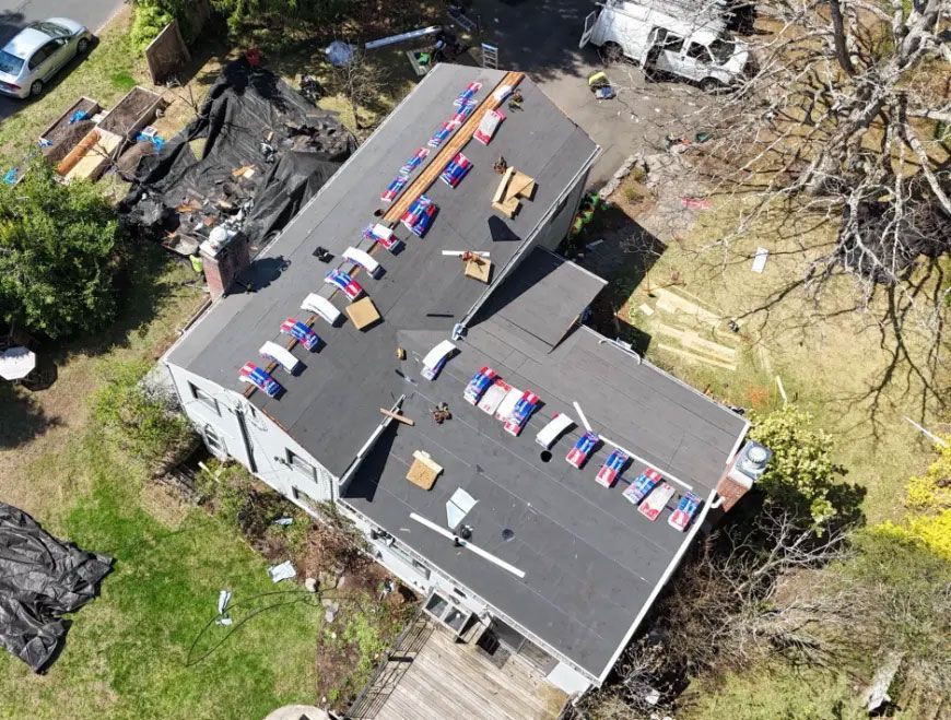 Aerial view of a house roof covered with rows of colorful debris after storm damage, with fallen trees nearby
