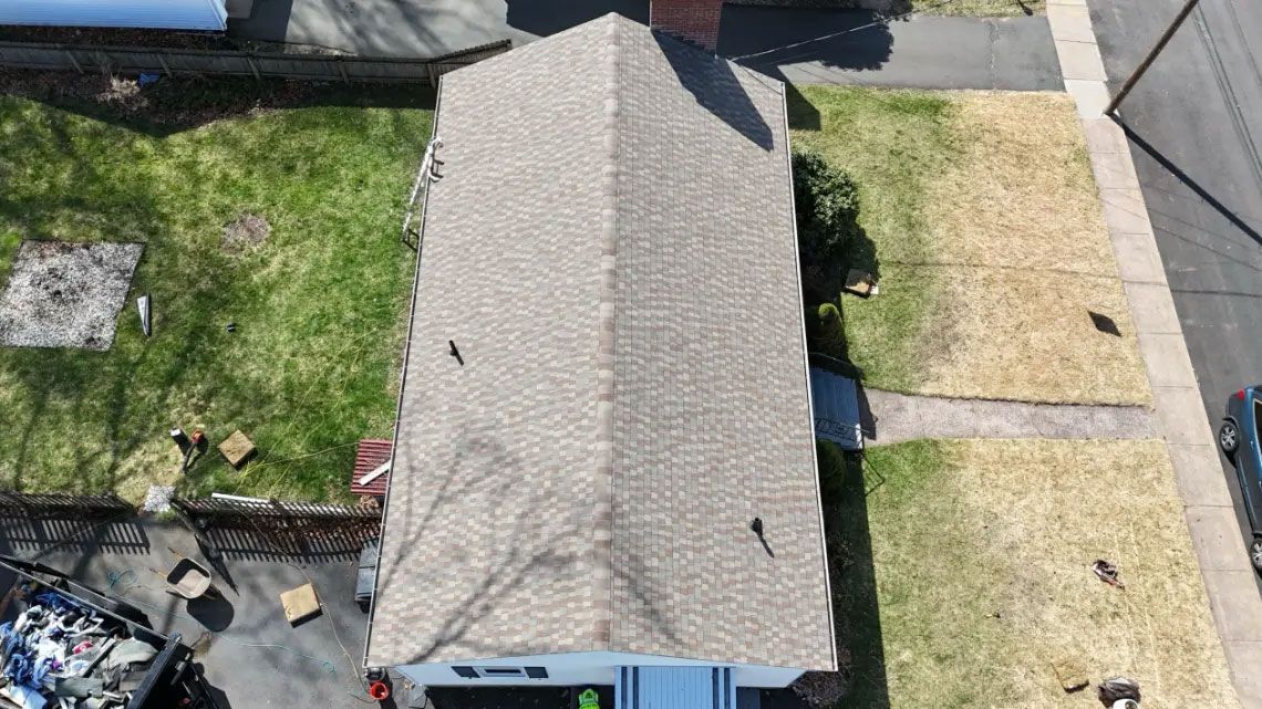 Aerial view of a house roof with adjacent yard, pavement, and driveway.