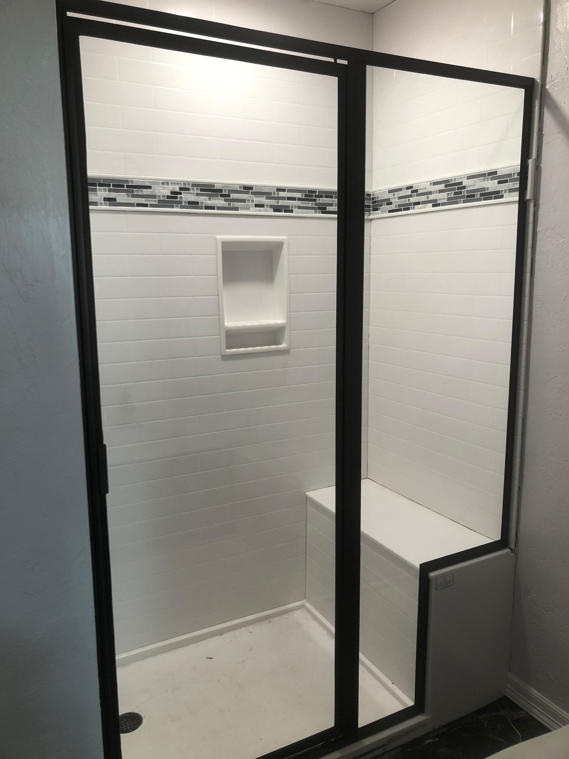 A bathroom with a walk in shower with a black frame and sliding glass doors.