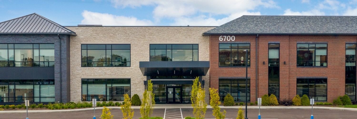 Exterior view of a modern office building with brick and stone facades, lush landscaping, and the address 