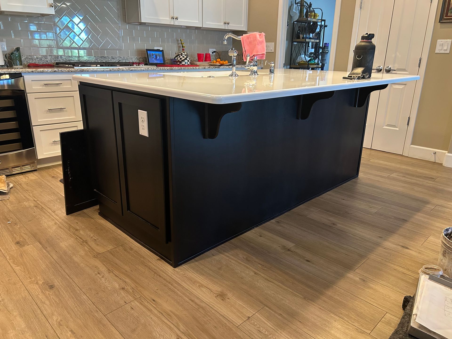 Modern kitchen with a large black island, white countertop, and wood-look flooring.