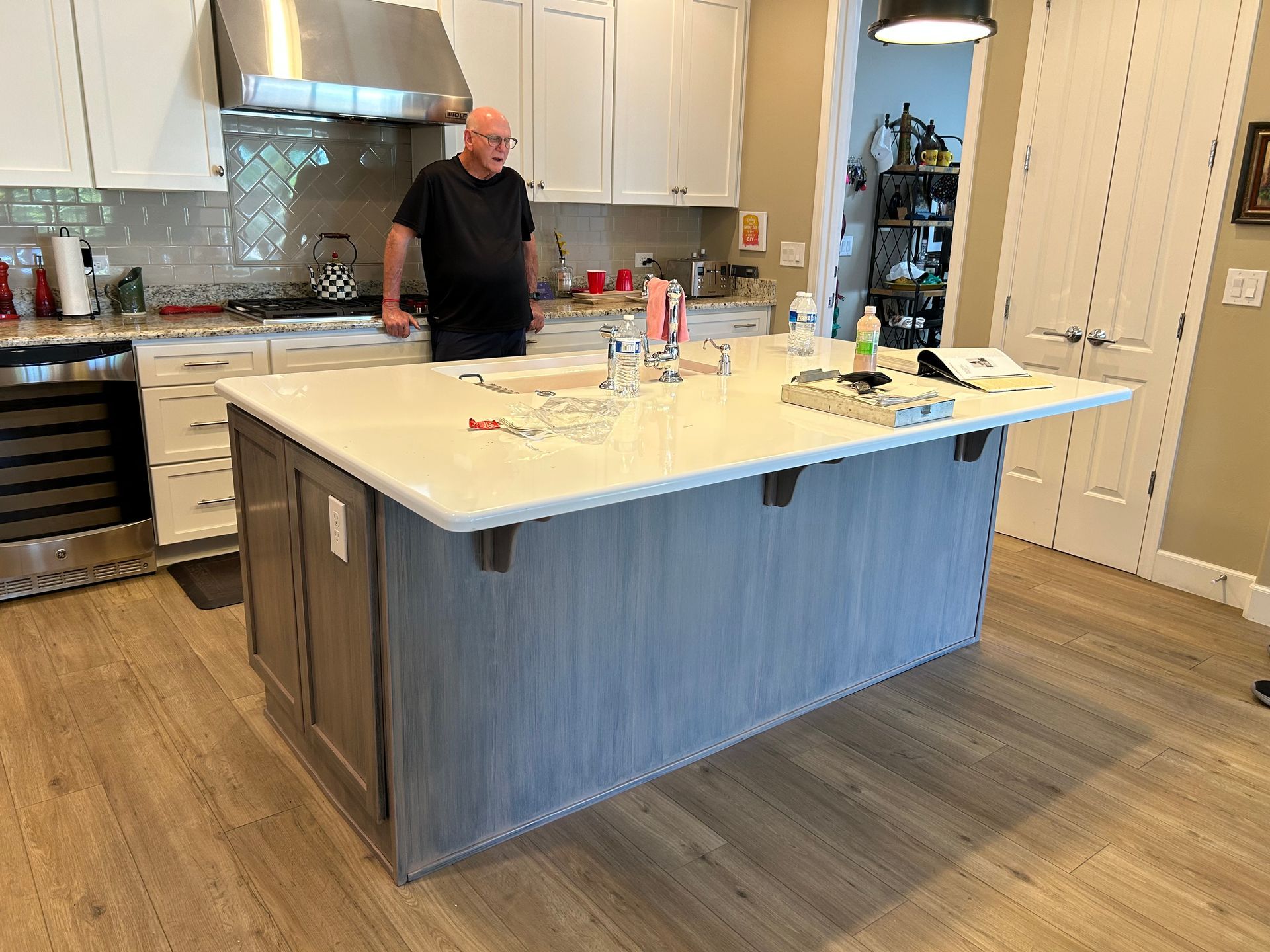 Modern kitchen with a large island, white cabinets, stainless hood, and a person standing near the counter.