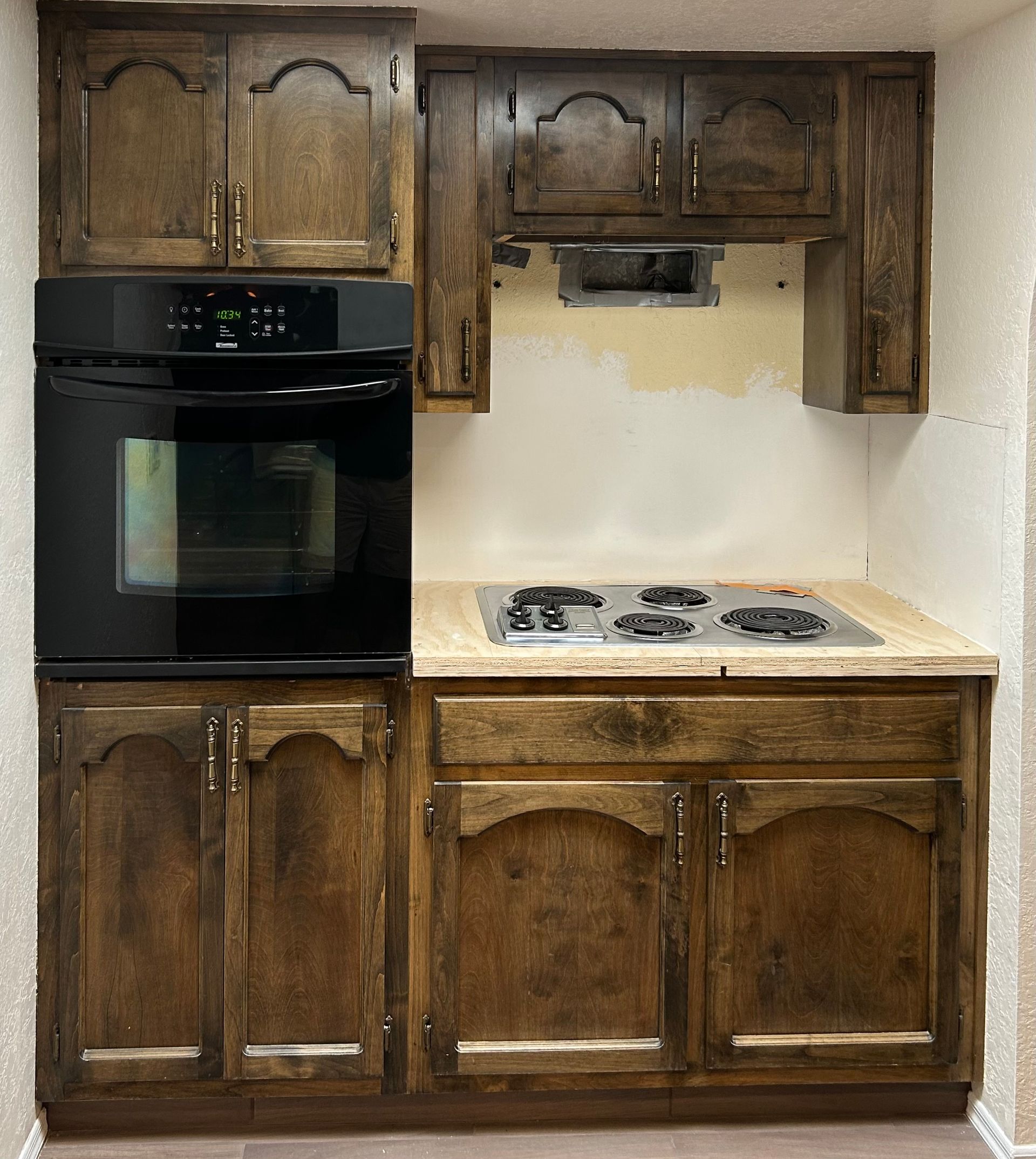 Small kitchen with dark wood cabinets, black wall oven, and white countertop with a stovetop.