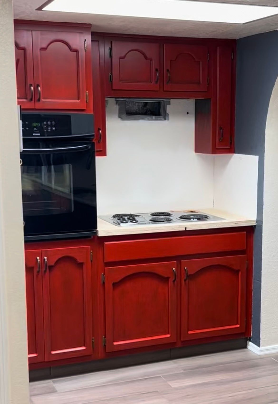 Red kitchen cabinetry with built-in oven, countertop stove, and white backsplash.