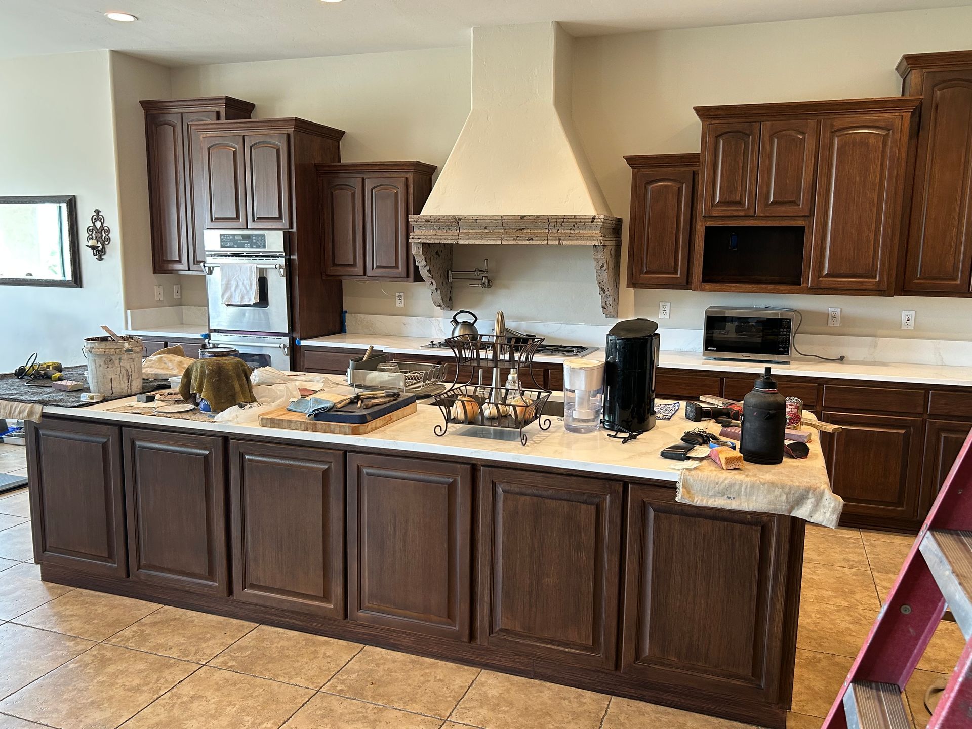 Large kitchen with dark wood cabinets, beige tile floor, and a long island covered in items.