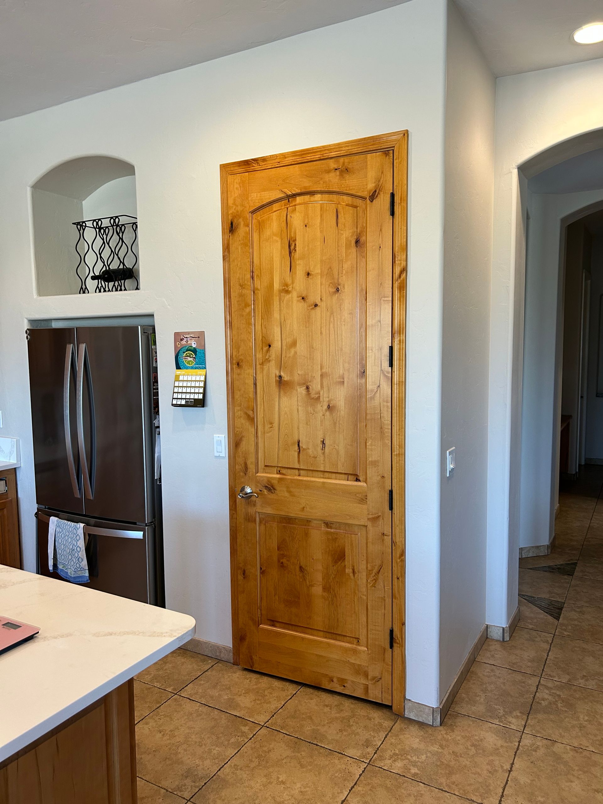 Kitchen with wooden pantry door, dark refrigerator, and tiled floor in a home interior.