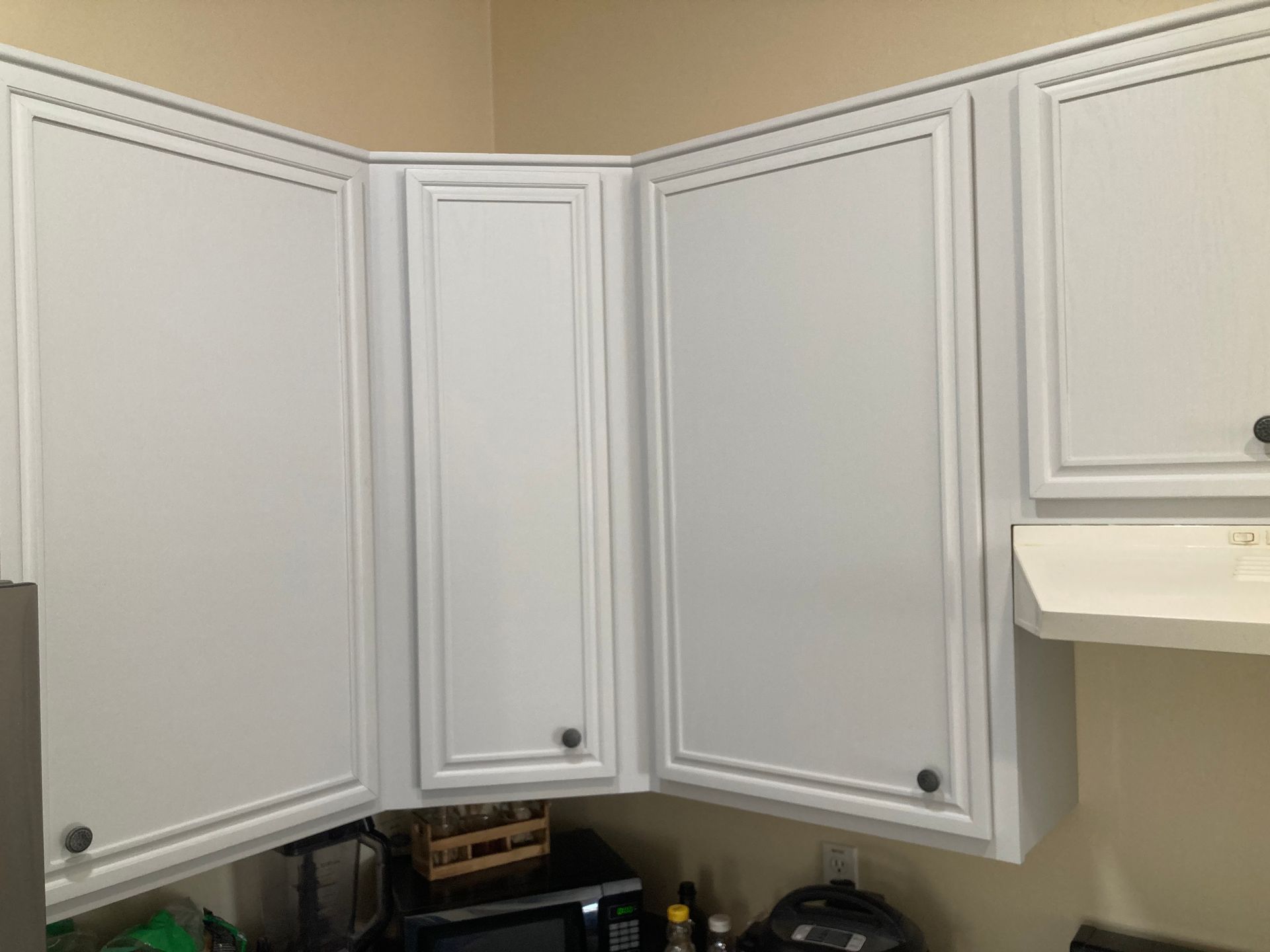 White kitchen cabinets with paneled doors and dark knobs above a countertop.
