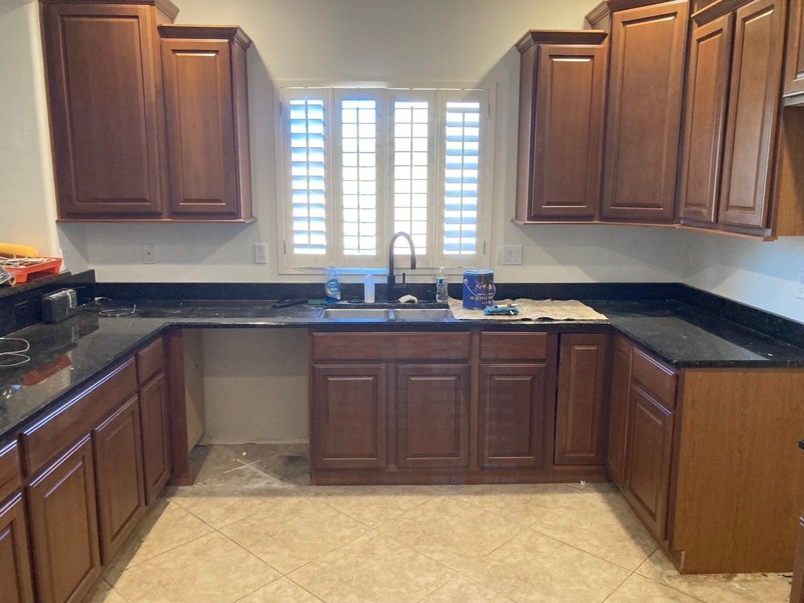 Kitchen with dark wood cabinets, black countertops, sink under a window, and beige tile floor.