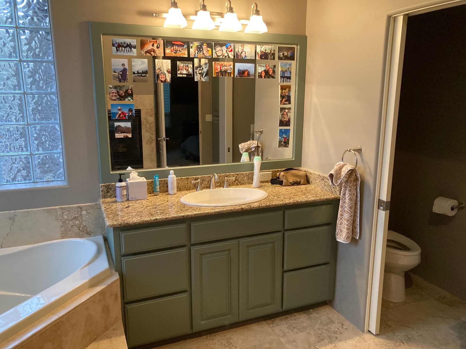 Bathroom vanity with granite countertop, mirror, sink, bathtub, and open toilet room in the background.