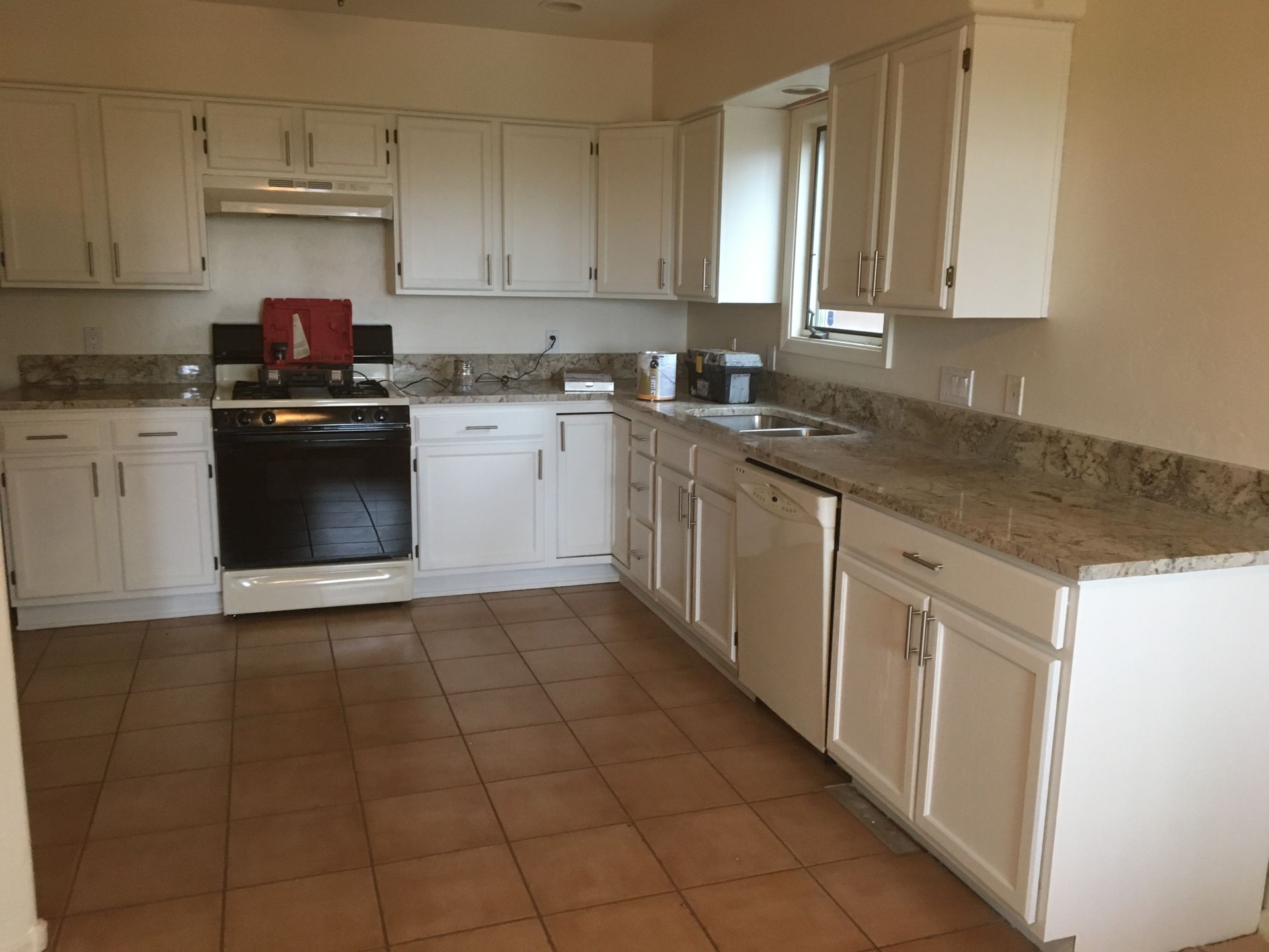 Empty kitchen with white cabinets, black stove, granite counters, and brown tile floor.
