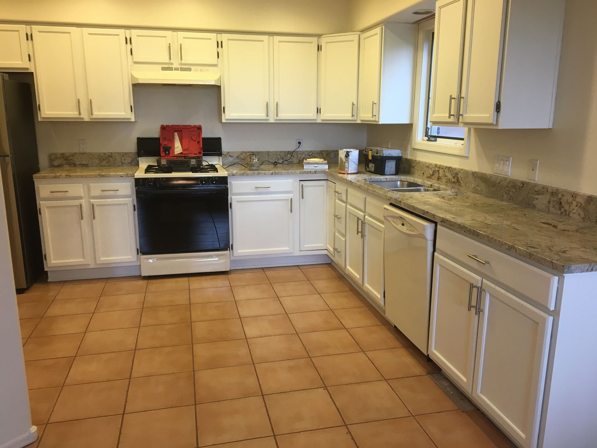 Bright kitchen with white cabinets, black stove, beige countertops, and tan tile floor.