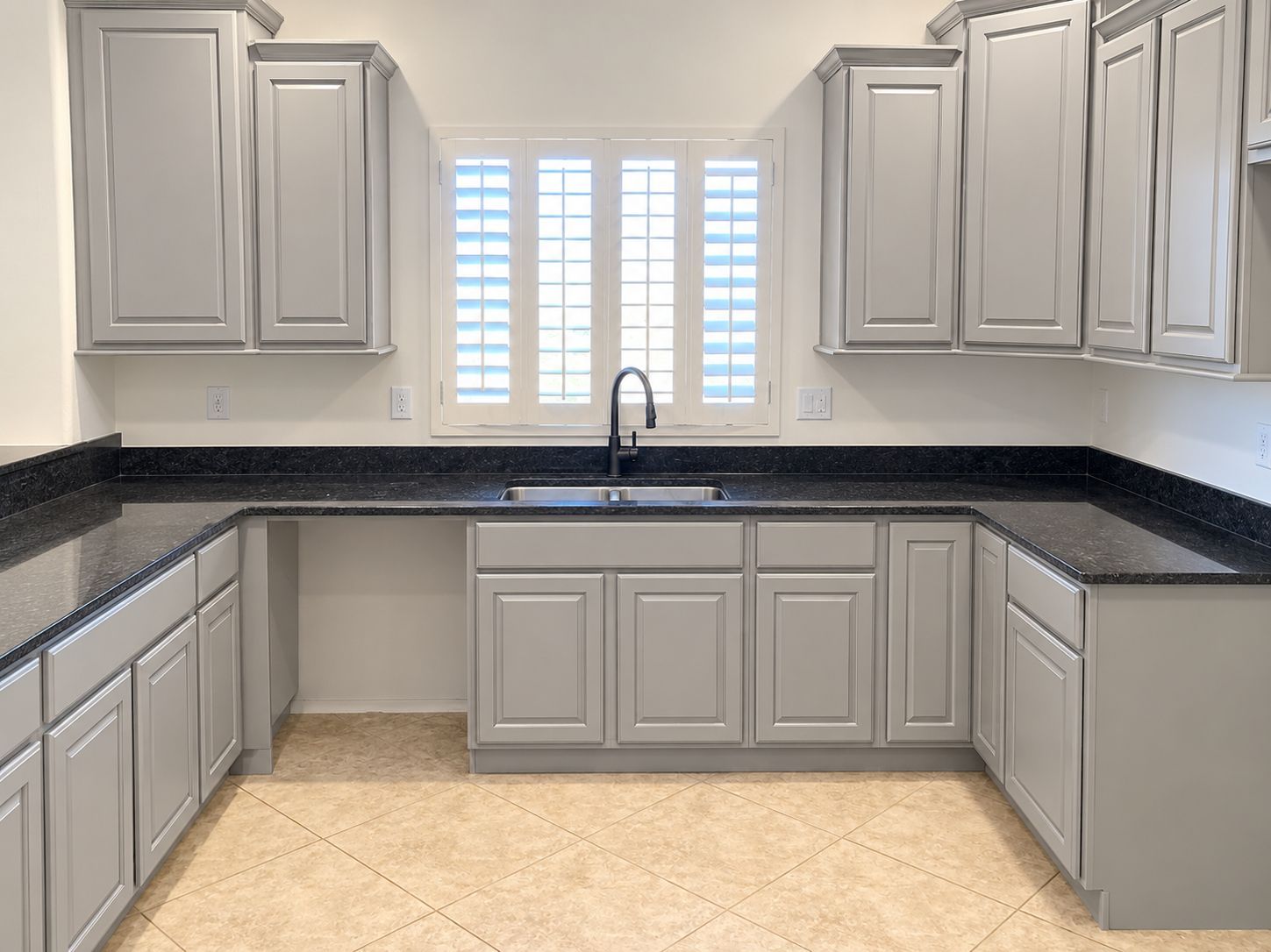 Bright kitchen with white cabinets, black countertops, tiled floor, and a window above the sink.