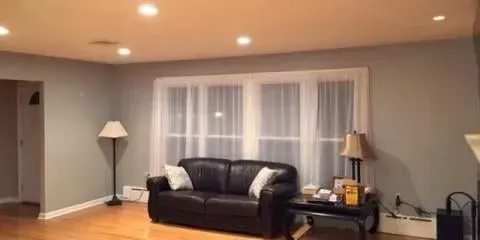 a living room with a black couch , two lamps , a table and a window